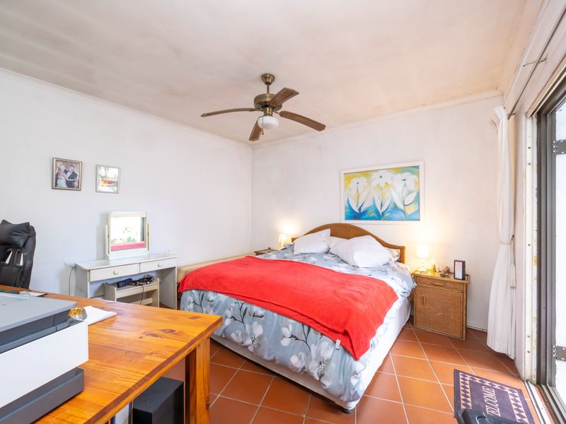 A bedroom featuring terracotta floor tiles, a ceiling fan, and a sliding glass door providing access to the exterior.