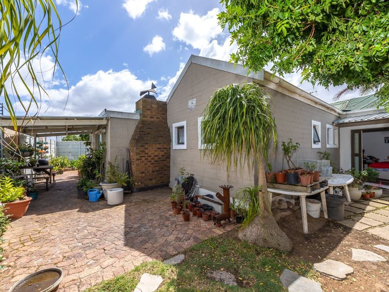 Rear exterior view of the property featuring a paved patio area, covered outdoor space, and a brick chimney stack.