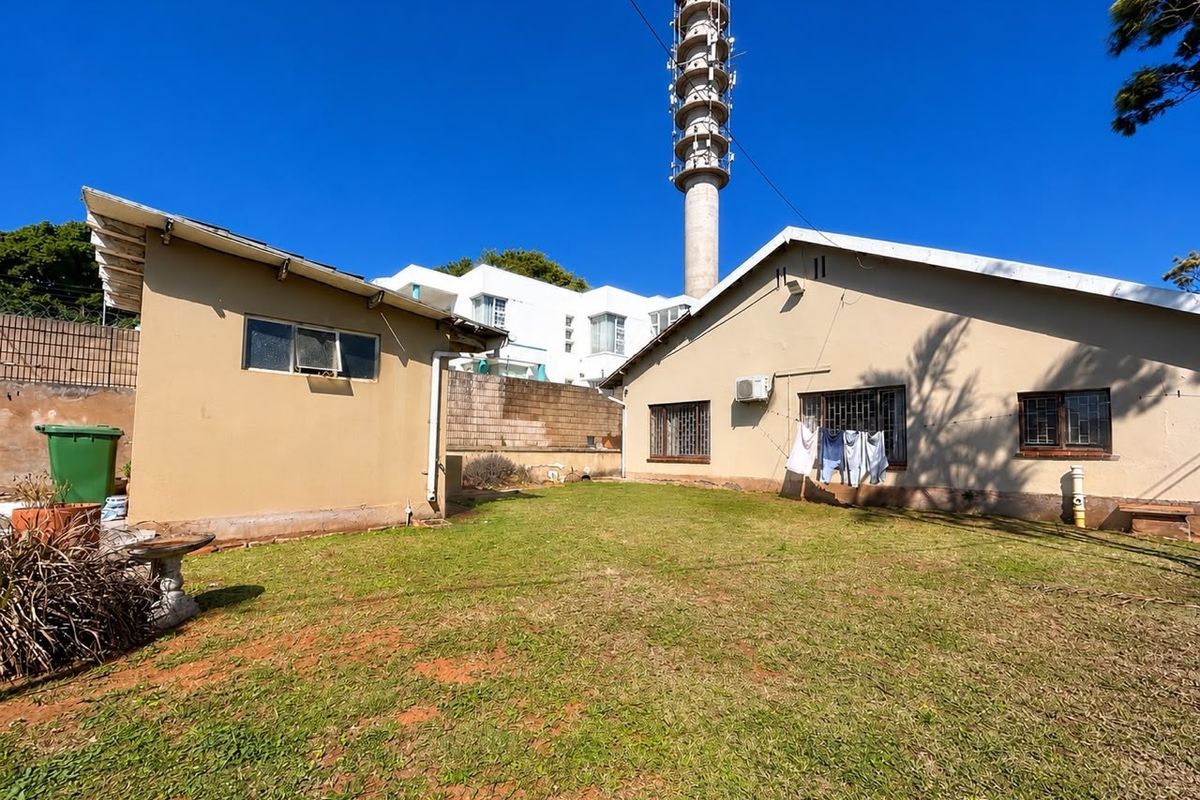 Rear garden area featuring a lawn, security-barred windows, and an external air conditioning unit, with a large telecommunications tower visible in the background.