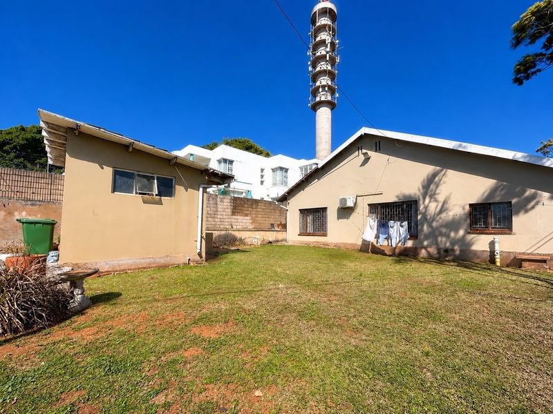 Rear garden area featuring a lawn, security-barred windows, and an external air conditioning unit, with a large telecommunications tower visible in the background.