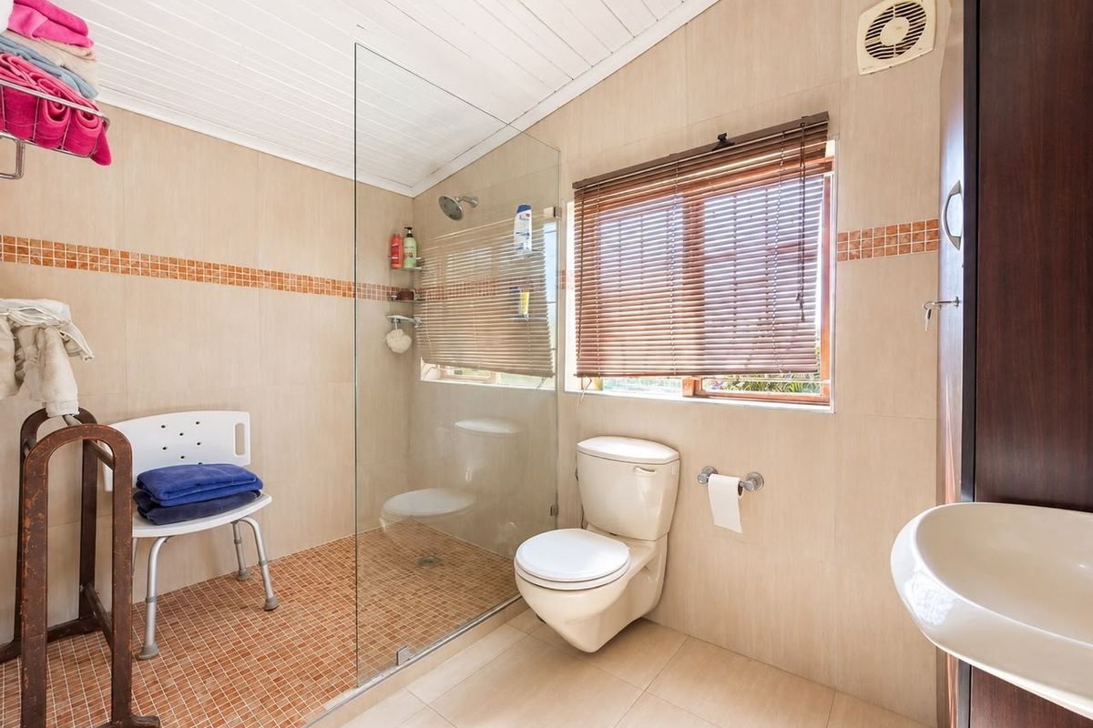 A functional bathroom featuring a walk-in shower with glass screen, toilet, washbasin, and neutral wall tiling with decorative mosaic accents.