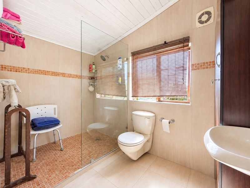 A functional bathroom featuring a walk-in shower with glass screen, toilet, washbasin, and neutral wall tiling with decorative mosaic accents.