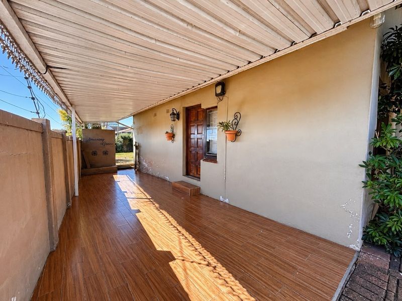 A covered patio area featuring wood-look tiled flooring, a corrugated metal roof, and direct access to the home through a timber door.