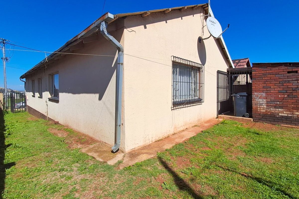 Rear exterior view of the house featuring a plastered facade, security bars on windows, and a brick boundary wall.