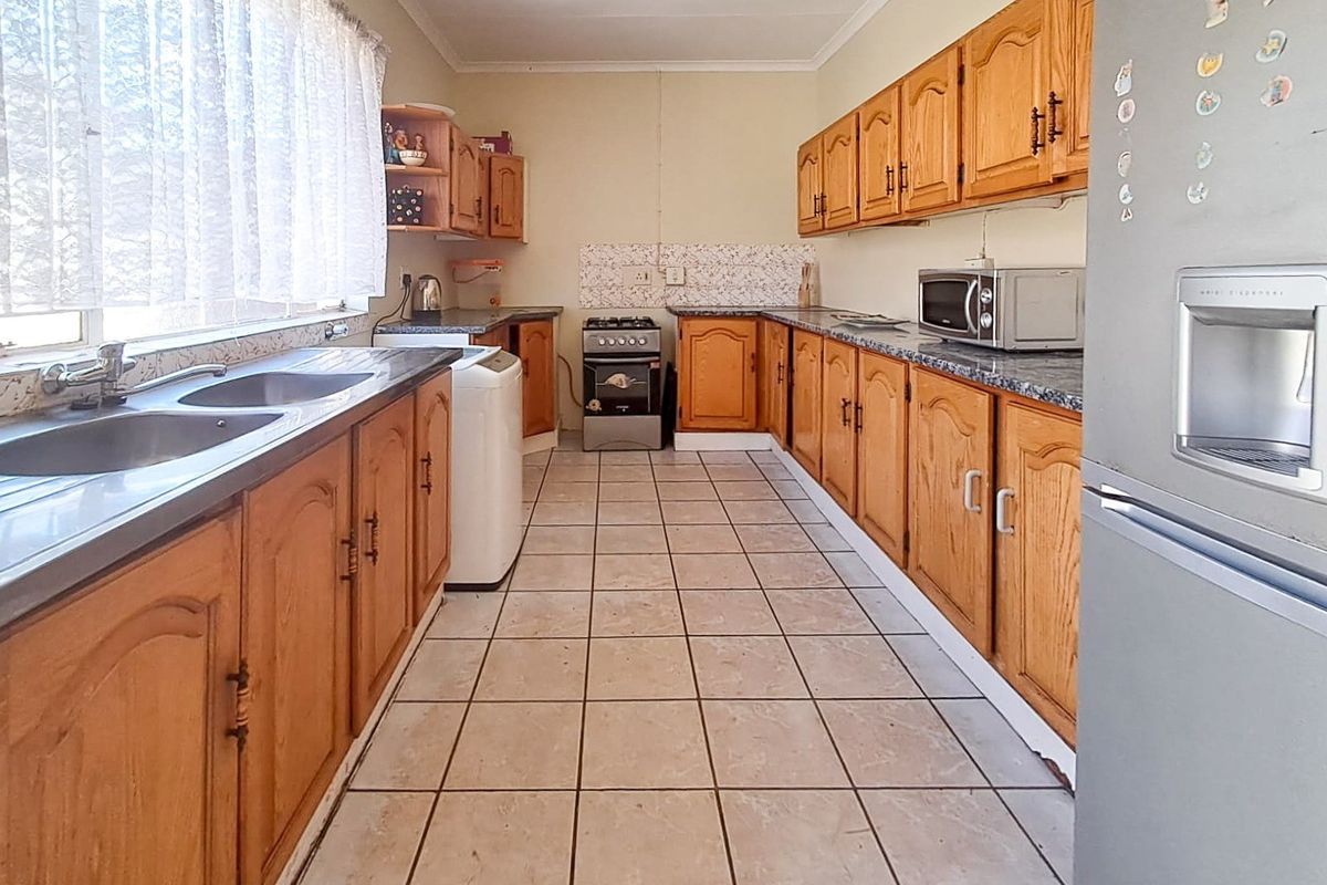 A functional kitchen featuring wooden cabinetry, laminate countertops, a double basin sink, and a freestanding gas stove with tiled flooring and backsplash.
