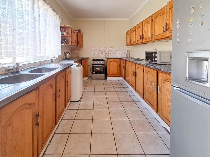A functional kitchen featuring wooden cabinetry, laminate countertops, a double basin sink, and a freestanding gas stove with tiled flooring and backsplash.