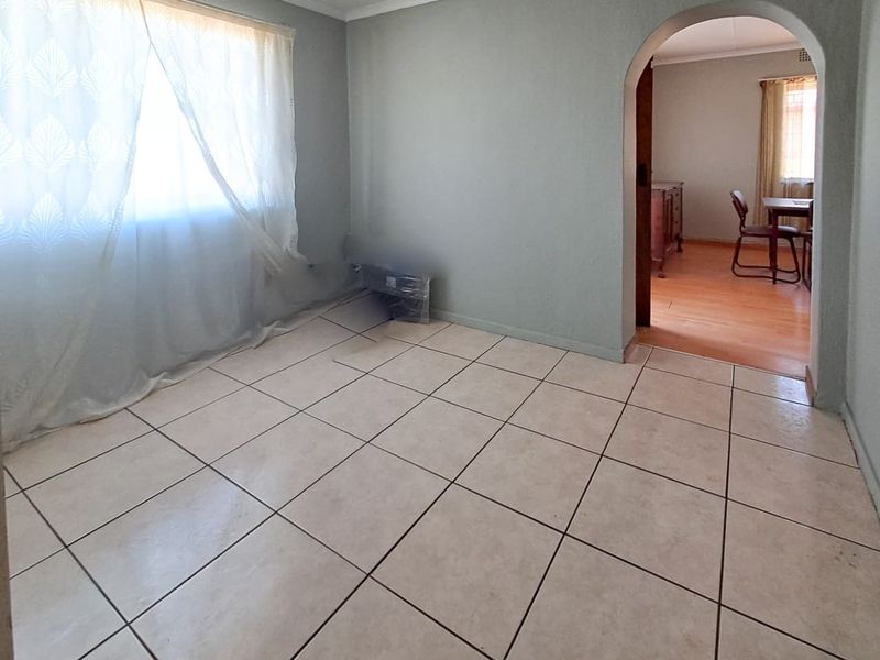 An empty living room featuring neutral tiled flooring and a classic arched doorway leading to an adjacent space.