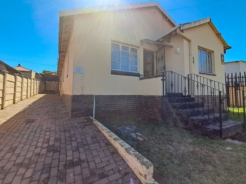 Front elevation of a single-story house featuring a paved driveway, concrete stairs with metal railings, and security bars on windows.