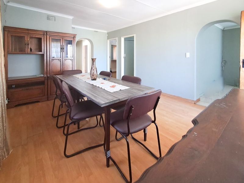 A dining room featuring laminate flooring, coved ceilings, and arched doorways leading to adjacent living spaces.