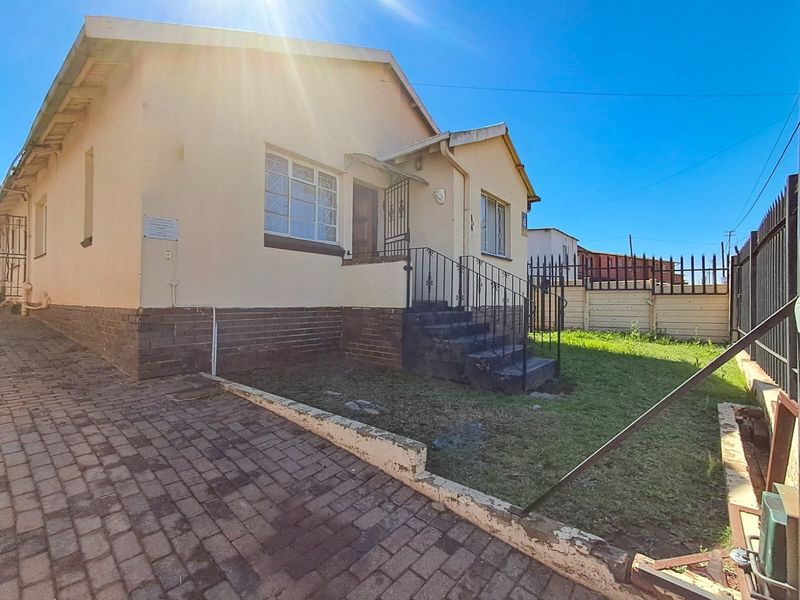 Front exterior view of a single-story house featuring a brick driveway, small front garden, and security features including metal bars and a wrought iron gate.