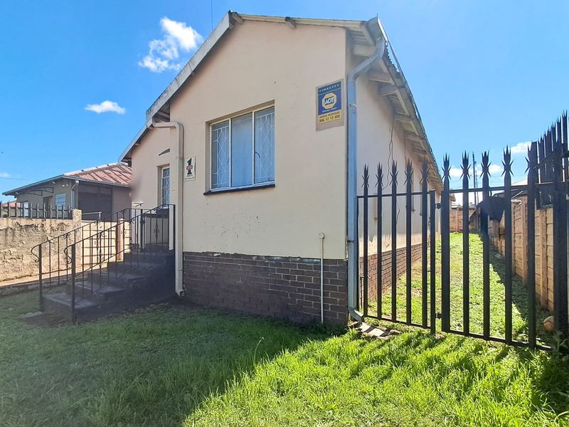 Front elevation of a detached house featuring a brick plinth, security fencing, and concrete entrance steps with wrought iron railings.