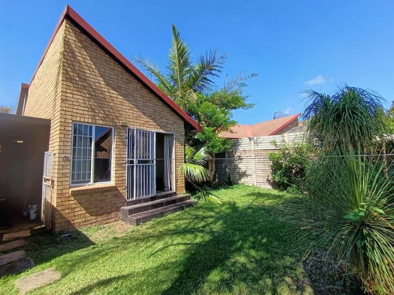 Rear view of the townhouse featuring a face brick facade, security gate access, tiled steps, and a private garden area with boundary walling.