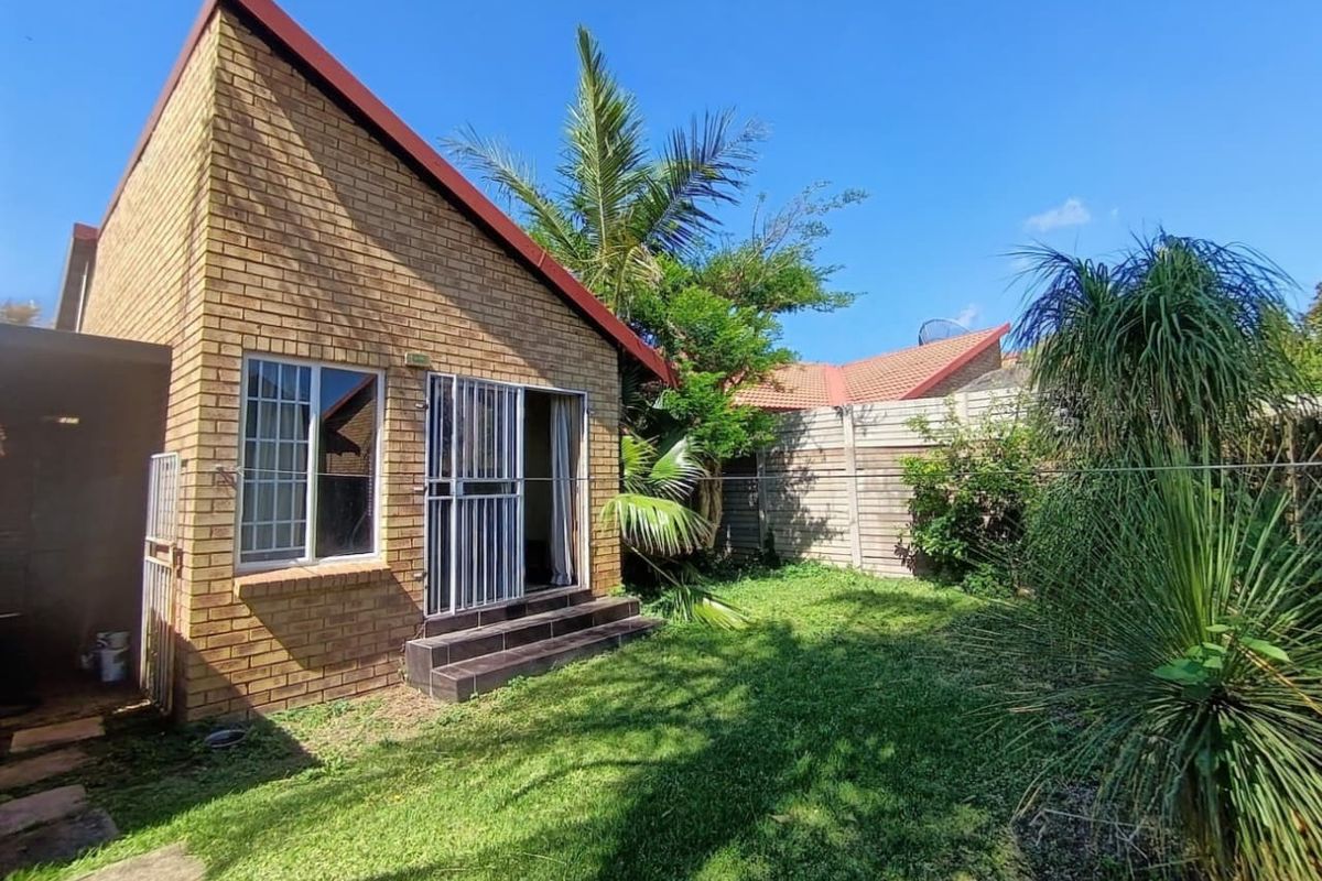Rear view of the townhouse featuring a face brick facade, security gate access, tiled steps, and a private garden area with boundary walling.