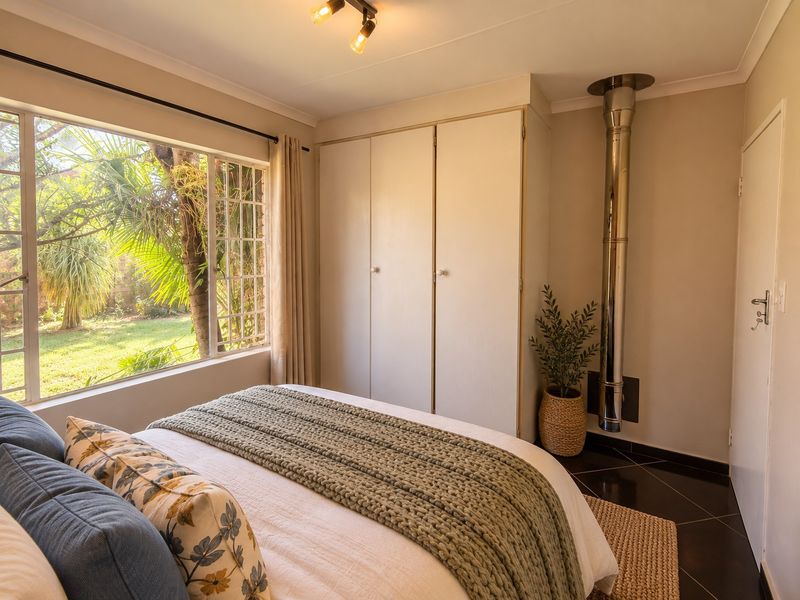 A well-lit bedroom featuring built-in cupboards, dark tiled flooring, and a prominent fireplace flue, offering a comfortable and functional living space.