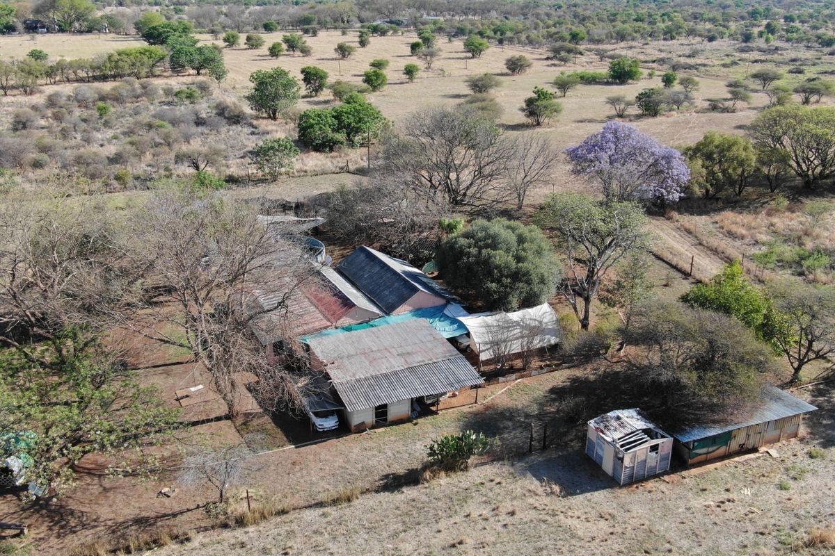 Aerial view of a small holding property featuring multiple structures with corrugated metal roofing and surrounding rural landscape.