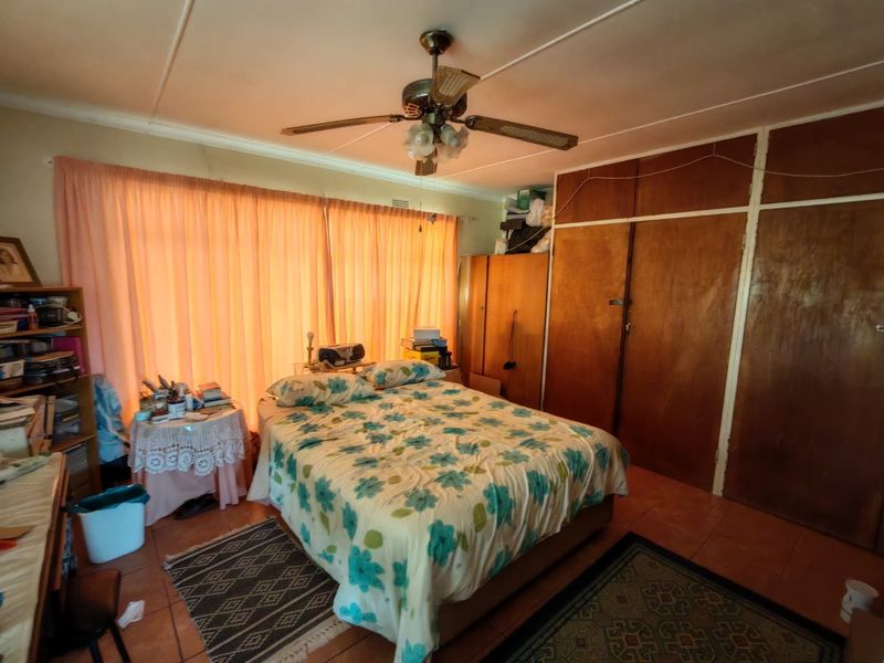 A bedroom featuring built-in wooden cupboards, a ceiling fan, and tiled flooring, offering a functional space with potential for modernization.