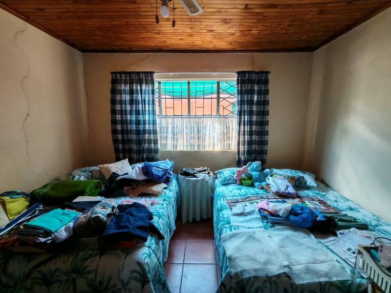 A bedroom featuring a timber ceiling, tiled floors, and security burglar bars on the window. Visible wall cracks indicate maintenance is required.