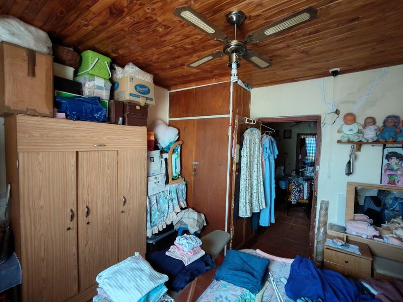 A bedroom featuring a wooden ceiling, ceiling fan, and built-in cupboards, showing signs of wear including cracked wall plaster.