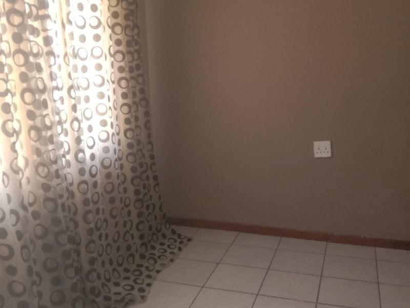 A clean, empty bedroom featuring neutral wall paint, tiled flooring, and a window with installed curtain tracks.