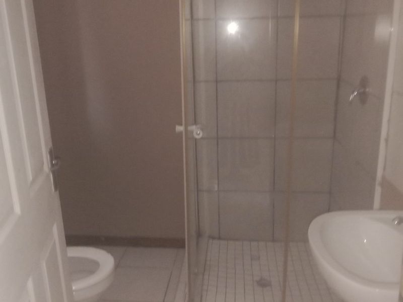 A functional bathroom featuring a shower enclosure, pedestal basin, and toilet with neutral tiled flooring and wall finishes.