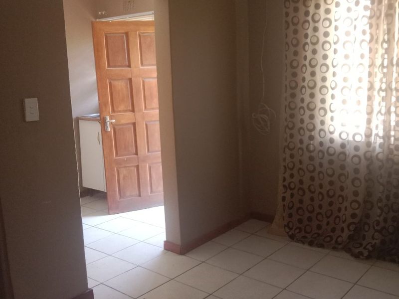 An empty living room featuring tiled flooring and neutral wall tones, with a doorway leading to an adjacent utility area.