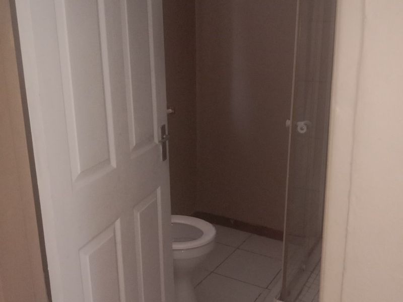 A functional bathroom featuring a shower enclosure and toilet with tiled flooring, presented in a clean, empty state.