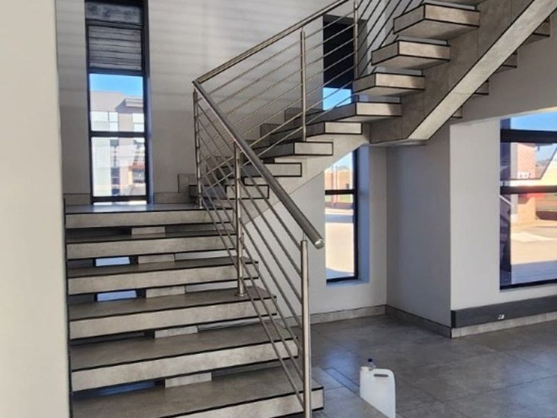Modern industrial entrance hall featuring a striking floating staircase with stainless steel balustrades, large windows, and high-quality tiled flooring in a double-volume space.