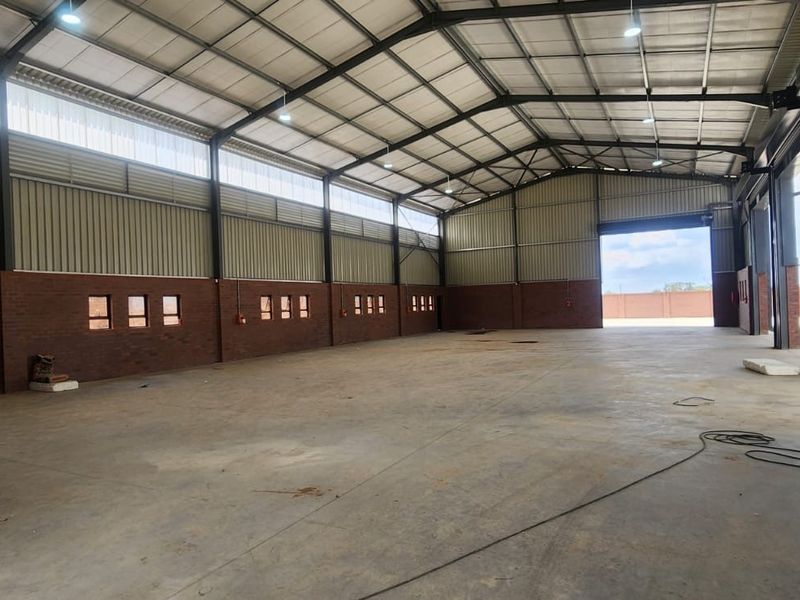Spacious industrial warehouse featuring a steel portal frame, concrete flooring, exposed brick walls, and high-bay lighting with large roller shutter access.