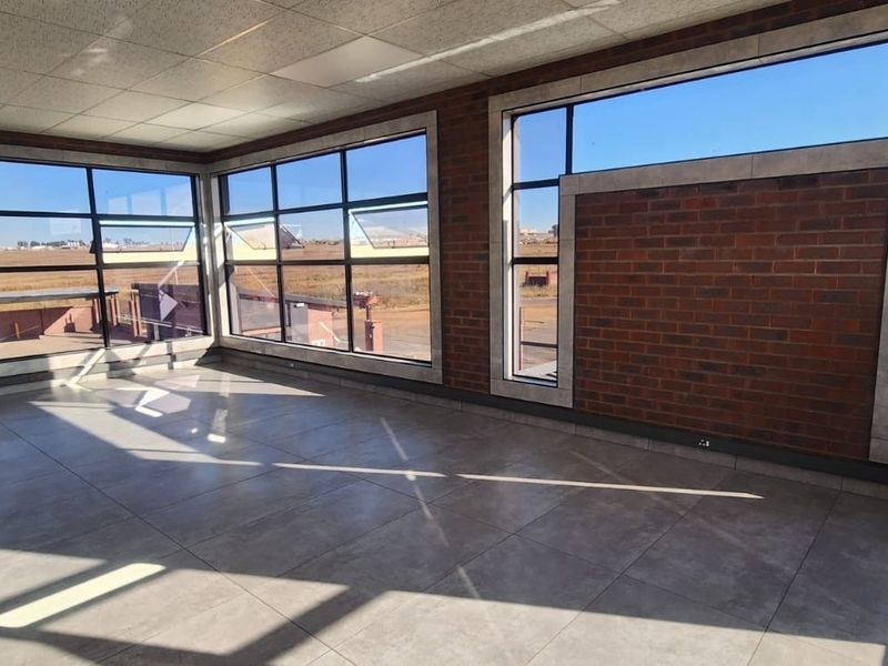 A bright, modern office space featuring large windows, exposed brick accents, and high-quality tiled flooring, offering an open and professional work environment.