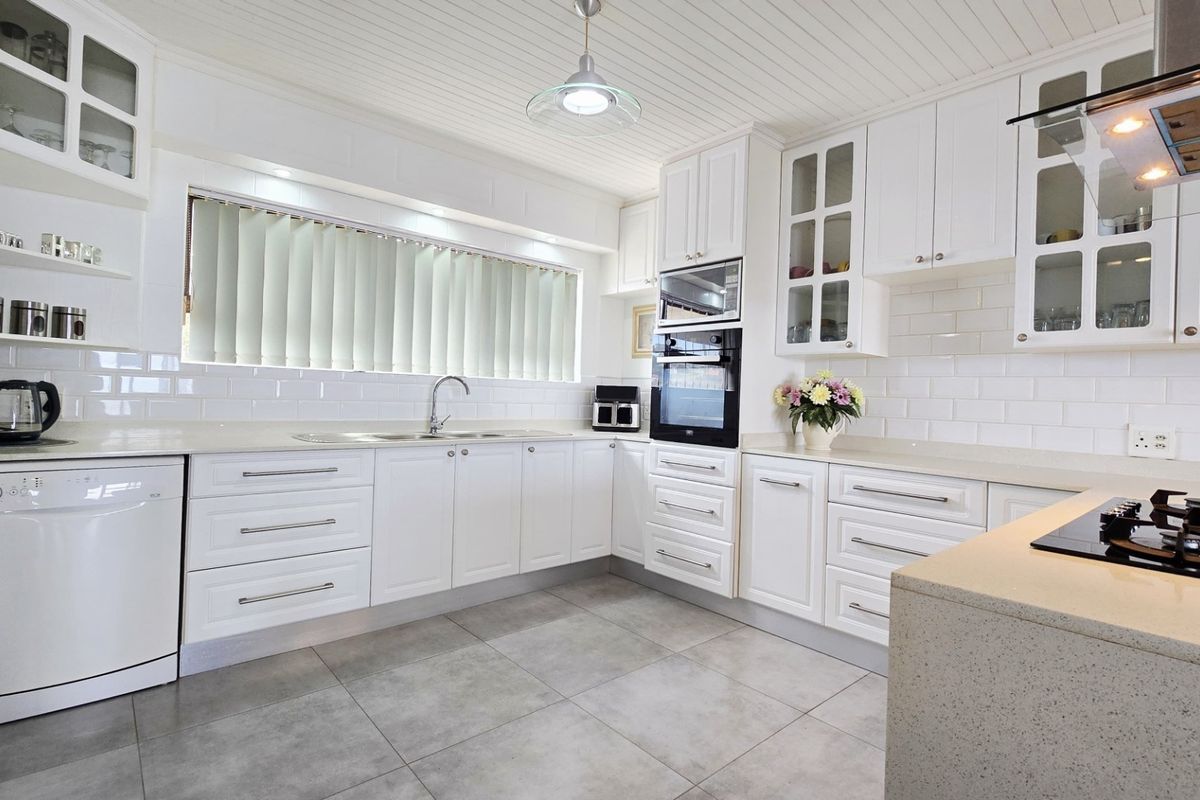 A well-maintained kitchen featuring white cabinetry, subway tile backsplash, stone countertops, and integrated appliances including an oven, microwave, and gas hob.