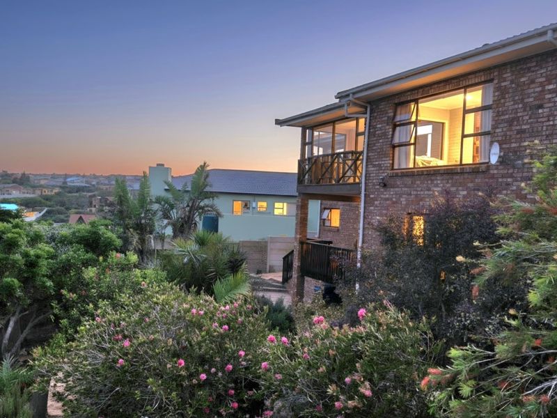 A rear view of a multi-story brick house at dusk, featuring a balcony with timber balustrades and established garden landscaping.