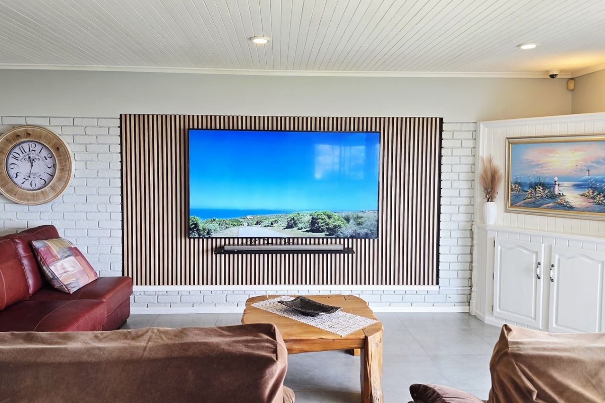 A well-maintained living room featuring a modern slatted timber accent wall, painted brickwork, and integrated cabinetry with recessed ceiling lighting.