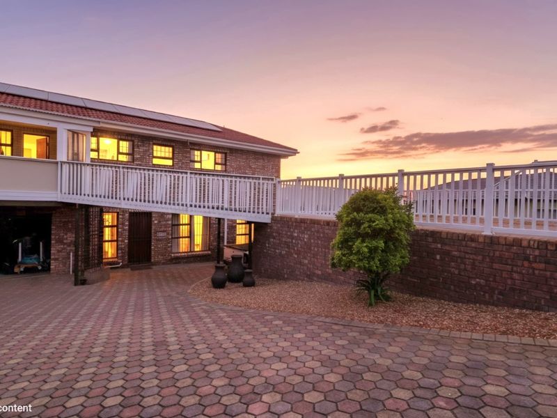 A well-maintained brick house featuring a paved driveway, raised balcony with white balustrade, and solar panels, captured during a scenic sunset.