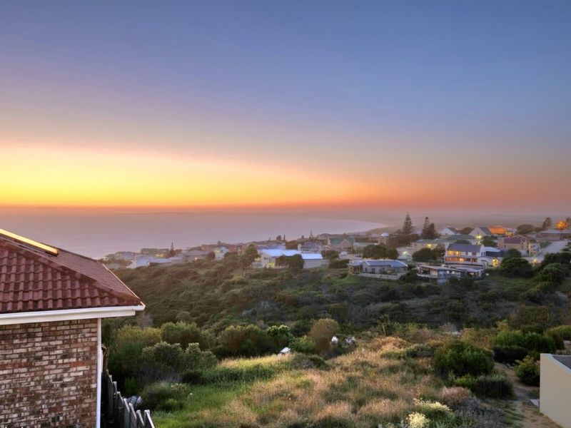 Elevated coastal view overlooking the surrounding residential area and coastline at sunset, featuring a property with a tiled roof and solar panels.