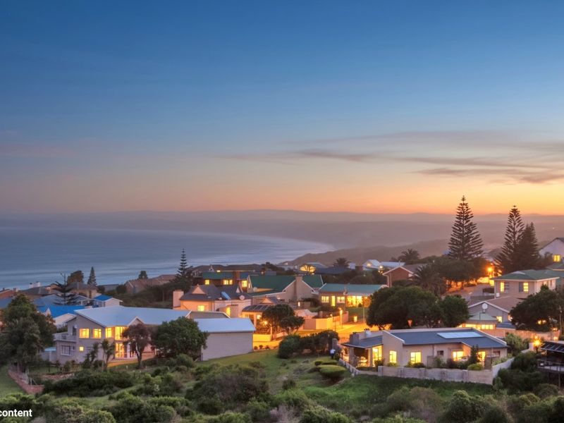 An elevated aerial view of a coastal residential neighborhood at dusk, showcasing the surrounding landscape and ocean horizon.