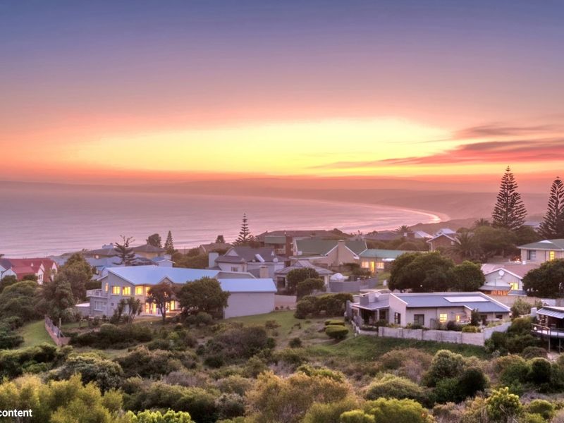 A scenic elevated view of a coastal residential neighborhood at sunset, showcasing the surrounding landscape and ocean horizon.