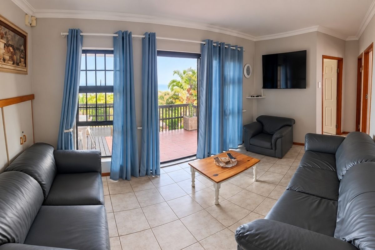 Spacious living room featuring tiled flooring, crown molding, and large sliding glass doors that open onto a balcony with scenic views.