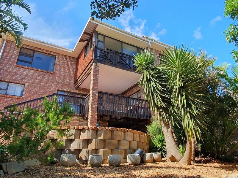Rear view of a multi-level brick house featuring a timber balcony, retaining wall, and established garden landscaping.