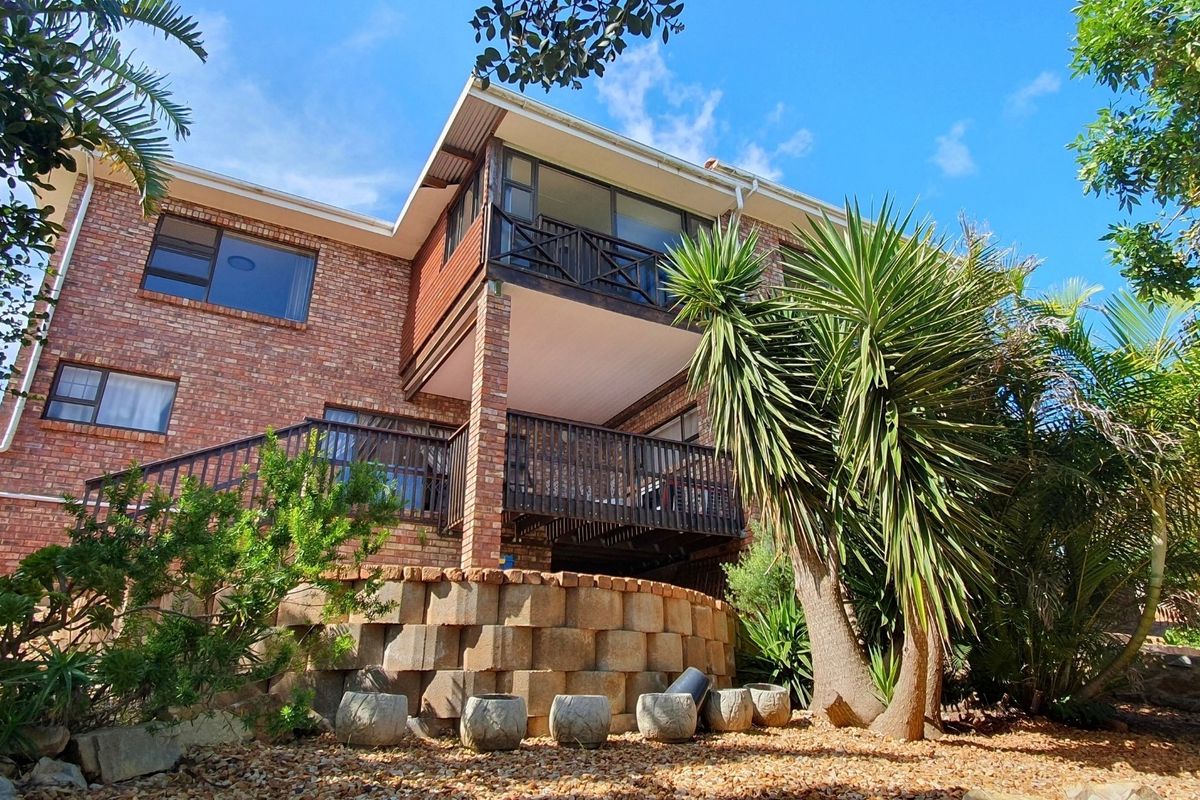 Rear view of a multi-level brick house featuring a timber balcony, retaining wall, and established garden landscaping.