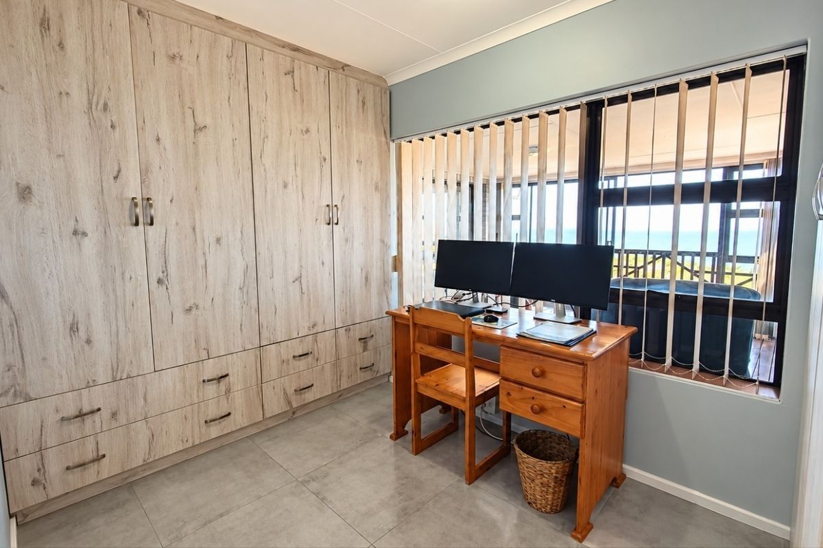 A well-maintained bedroom featuring extensive built-in wooden cabinetry, neutral floor tiles, and a large window with vertical blinds providing natural light.