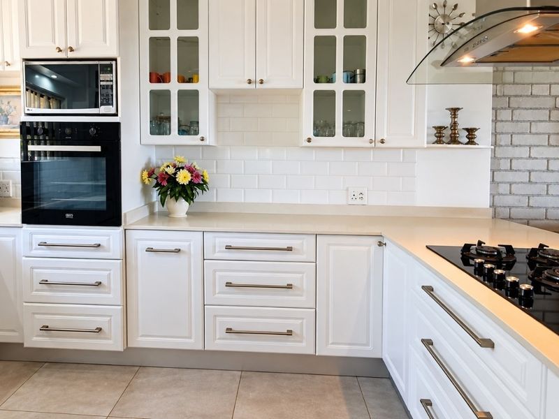 Modern kitchen featuring white shaker-style cabinetry, stone countertops, subway tile backsplash, built-in appliances, and a distinctive brick feature wall.