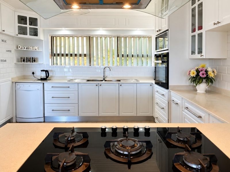 A well-appointed kitchen featuring white cabinetry, subway tile backsplash, stone countertops, a gas cooktop, and integrated appliances.