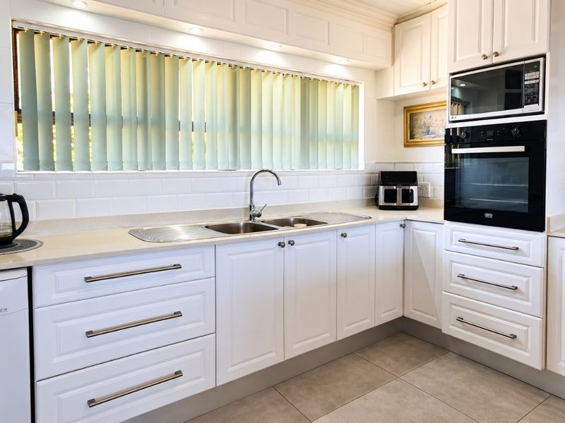 A well-maintained kitchen featuring white shaker-style cabinetry, stone countertops, a subway tile backsplash, and integrated appliances including an oven and microwave.