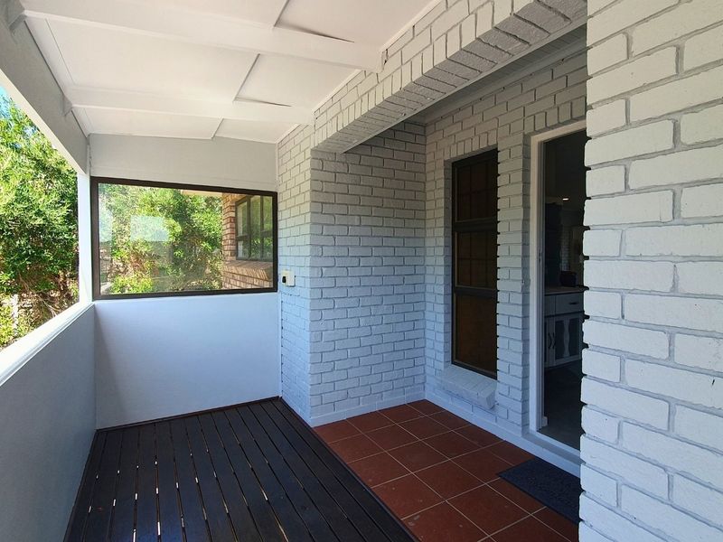 A well-maintained covered patio featuring a combination of timber decking and tiled flooring, with painted brick walls and a clean, neutral aesthetic.