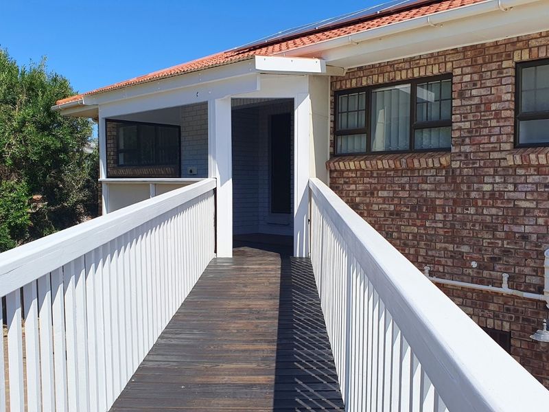 An elevated timber walkway leading to the entrance of a brick-faced home, featuring white balustrades and a tiled roof.