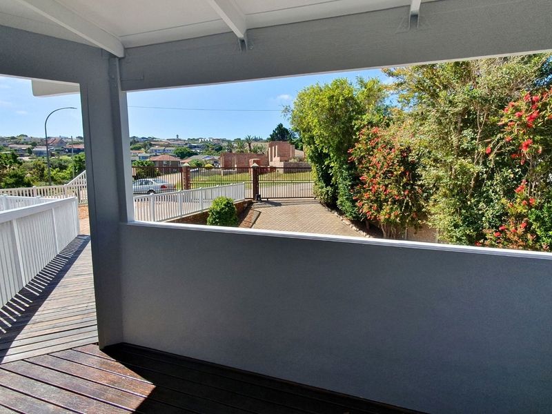 A covered balcony featuring timber decking and white railings, offering an elevated view of the driveway and surrounding neighbourhood.
