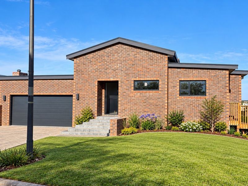 Modern single-story brick home featuring a double garage, paved driveway, landscaped front garden, and a raised timber deck entrance.