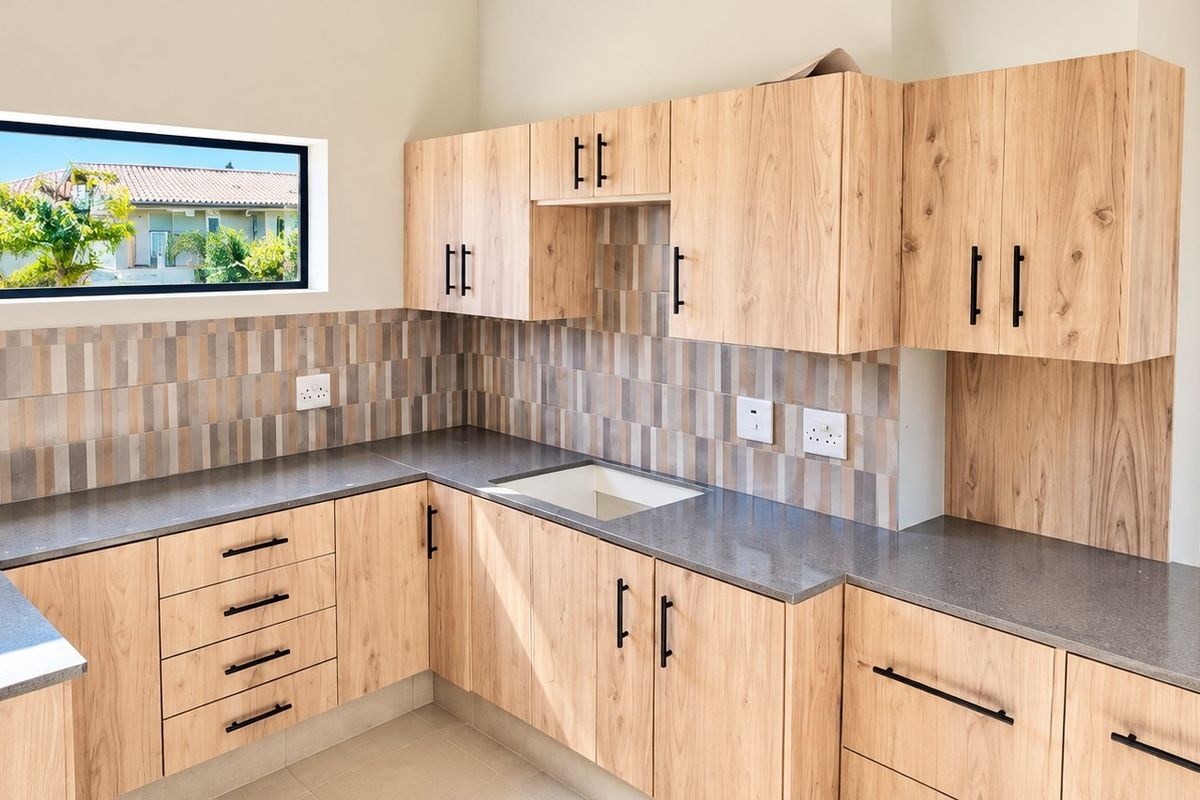 Modern kitchen featuring light wood-look cabinetry, stone-look countertops, a tiled backsplash, and a horizontal window providing natural light.