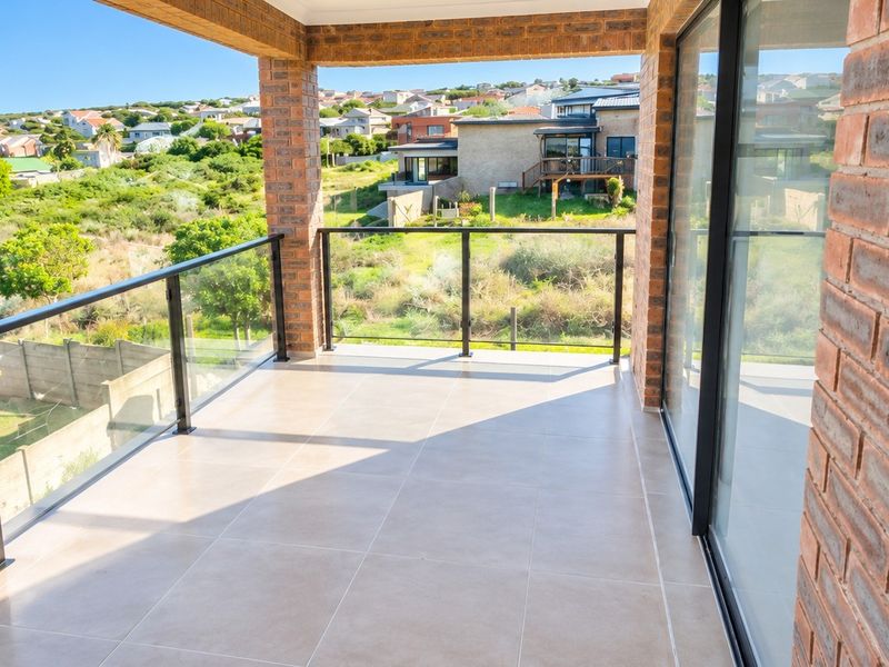 A modern covered balcony featuring tiled flooring, exposed brick pillars, and a glass balustrade, offering elevated views of the surrounding neighborhood.