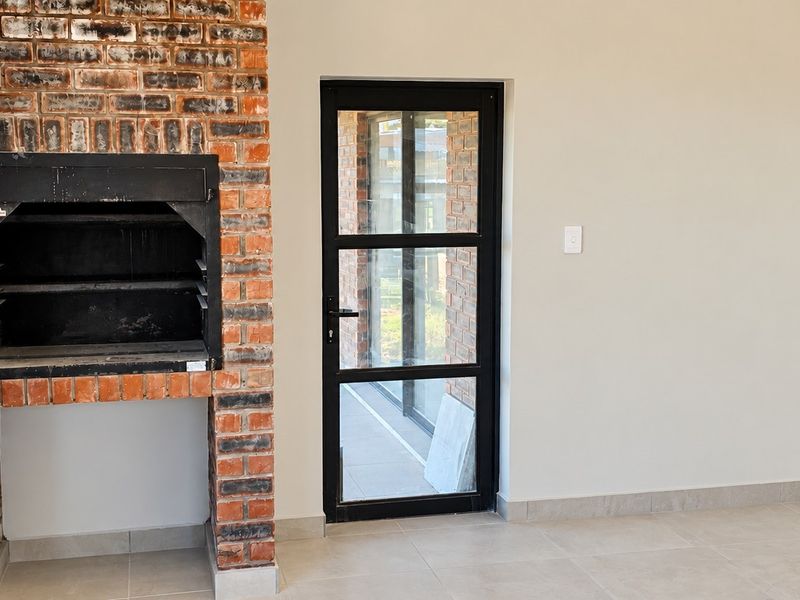 A bright, modern living area featuring a built-in brick fireplace and a sleek black-framed glass door leading to the exterior.